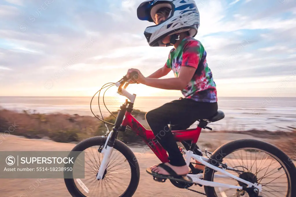 Young boy riding his bike on a coastal trail at sunset.