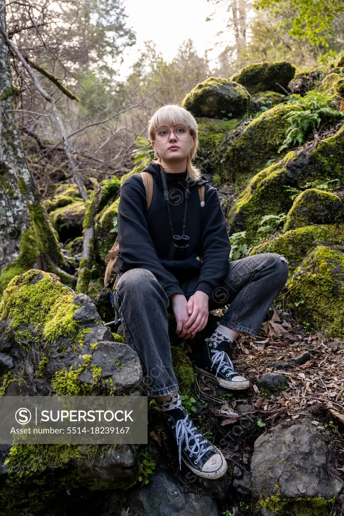 Young hiker sitting on mossy stones taking break looking calm