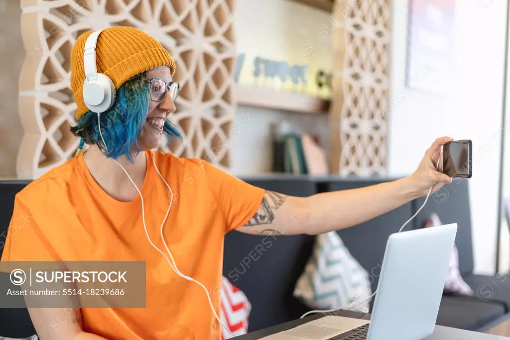 Modern young woman making selfie with smartphone and headphones