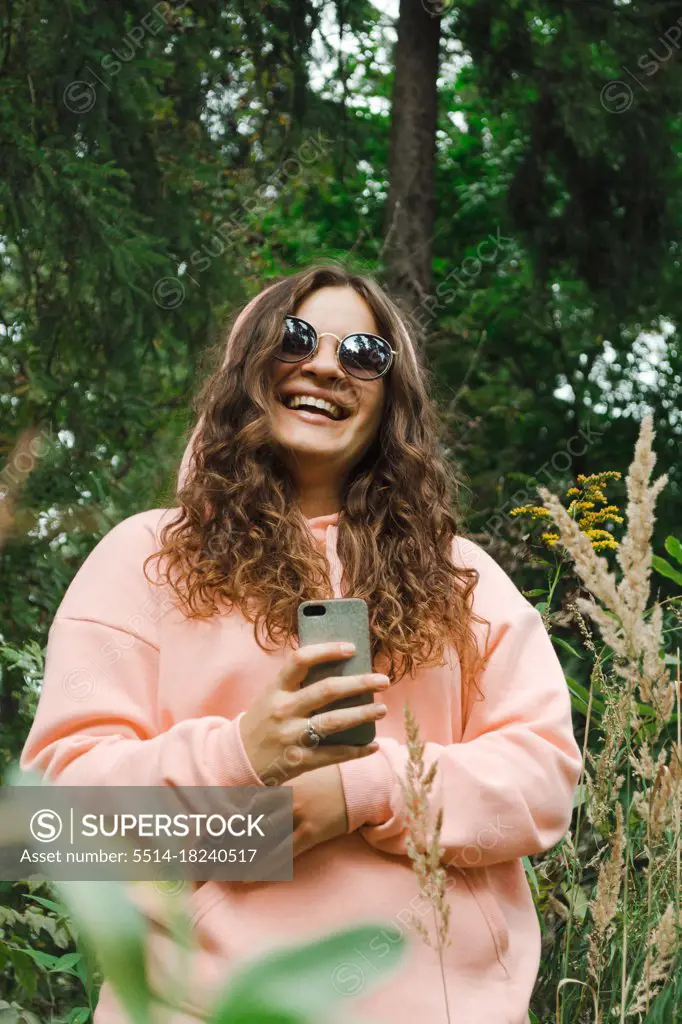 A young woman in a pink sweatshirt, in sunglasses, with a phone, laugh