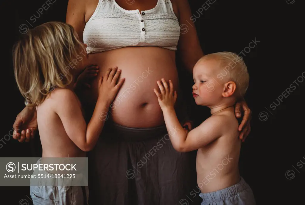 Young happy children hugging touching mom's pregnant big belly at home