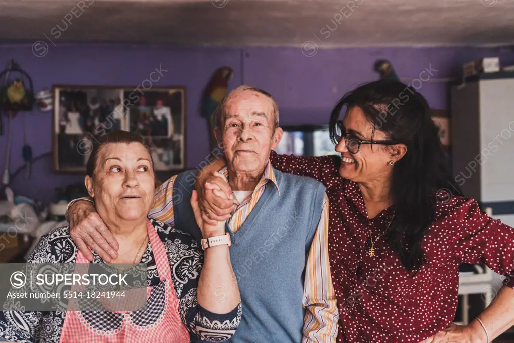 Portrait of a middle-aged daughter and her elderly parents hugging and smiling.