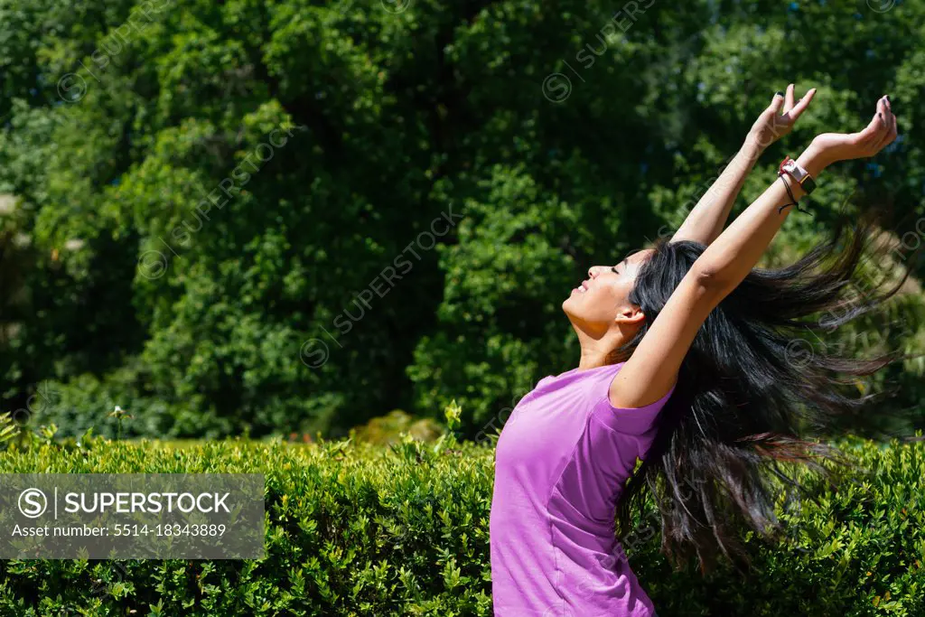 Young cheerful woman dancing outdoor. She is raising her arms on air.