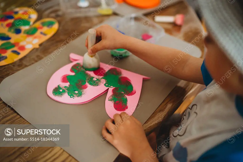 Close up of child hands painting colorful butterfly with sponge stamps