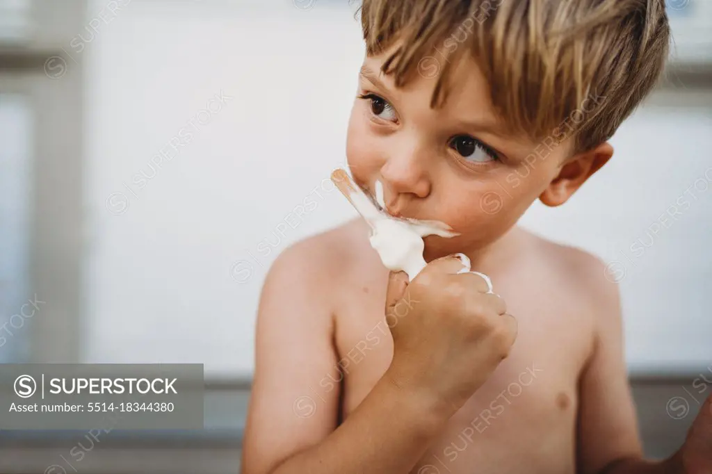 Cute young boy eating ice cream looking to the side outside in summer