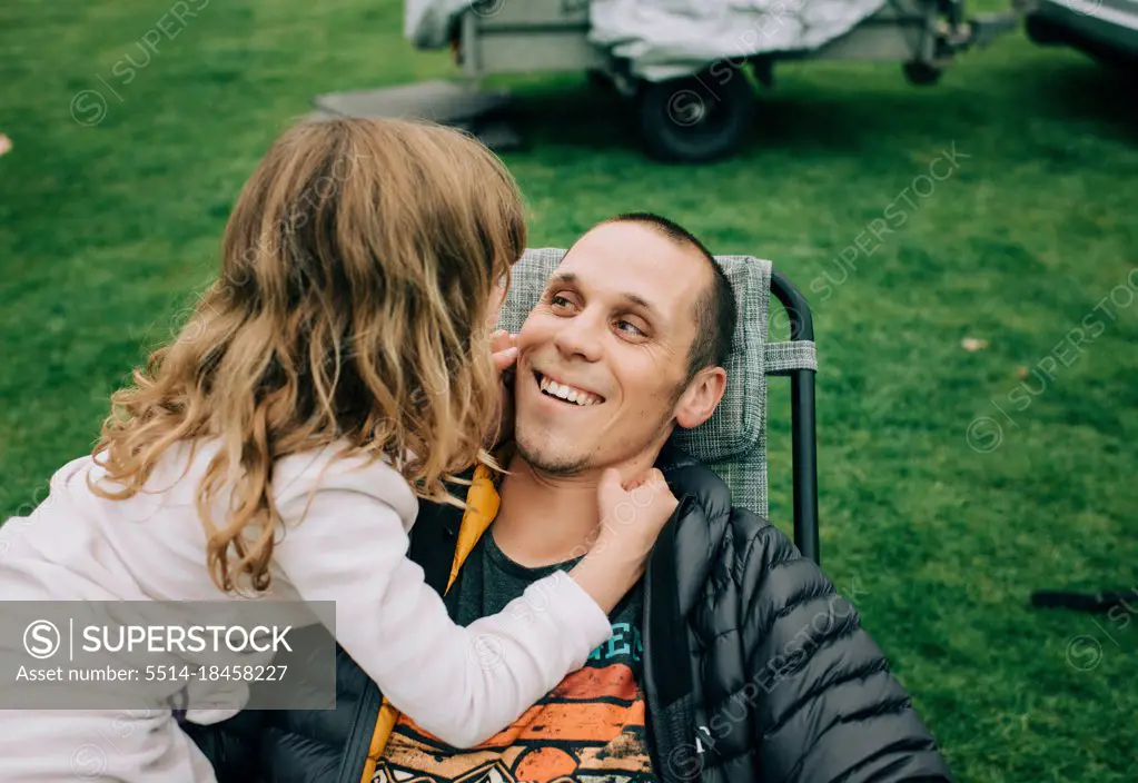 child playing with dads cheeks making him smile whilst camping