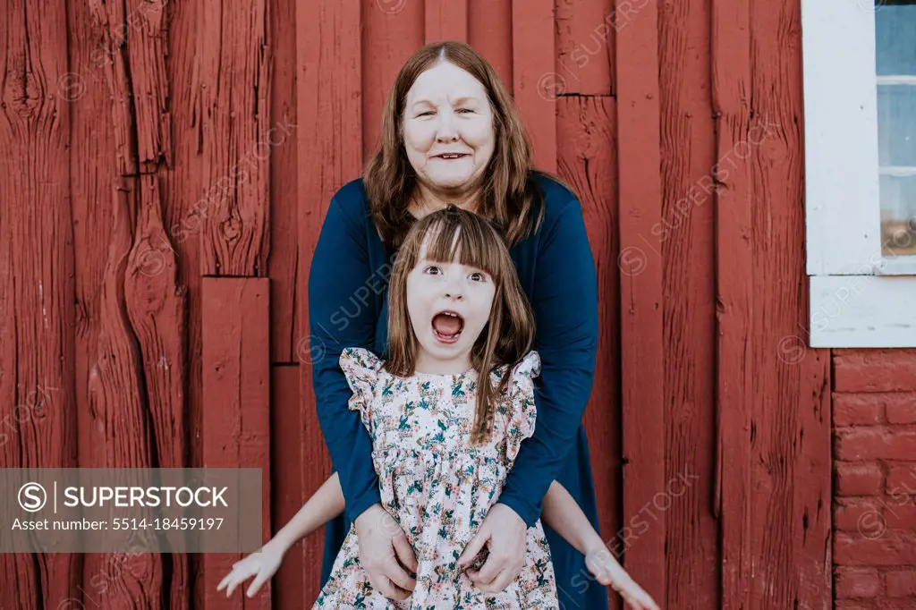 Grandma tickling happy grand daughter in front of red barn