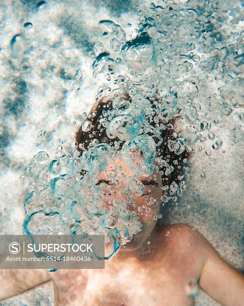 Underwater image of teenage boy blowing bubbles in a pool.