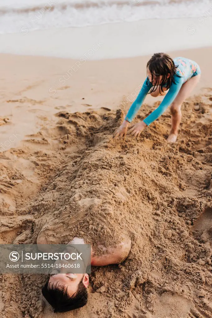 Daughter buries dad in the sand on Waikiki beach during sunset