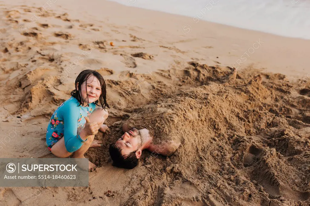 Young girl gives thumbs up after burying dad in sand on Waikiki beach