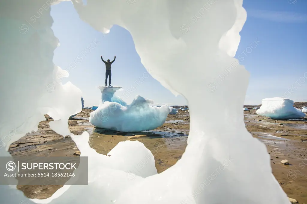 Man standing on top of iceberg, arms raised, Baffin Island.