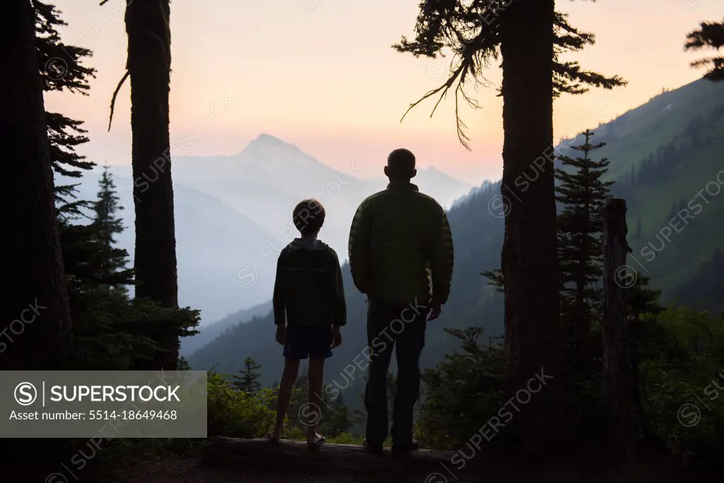 A boy and his dad enjoy the sunset together while camping.