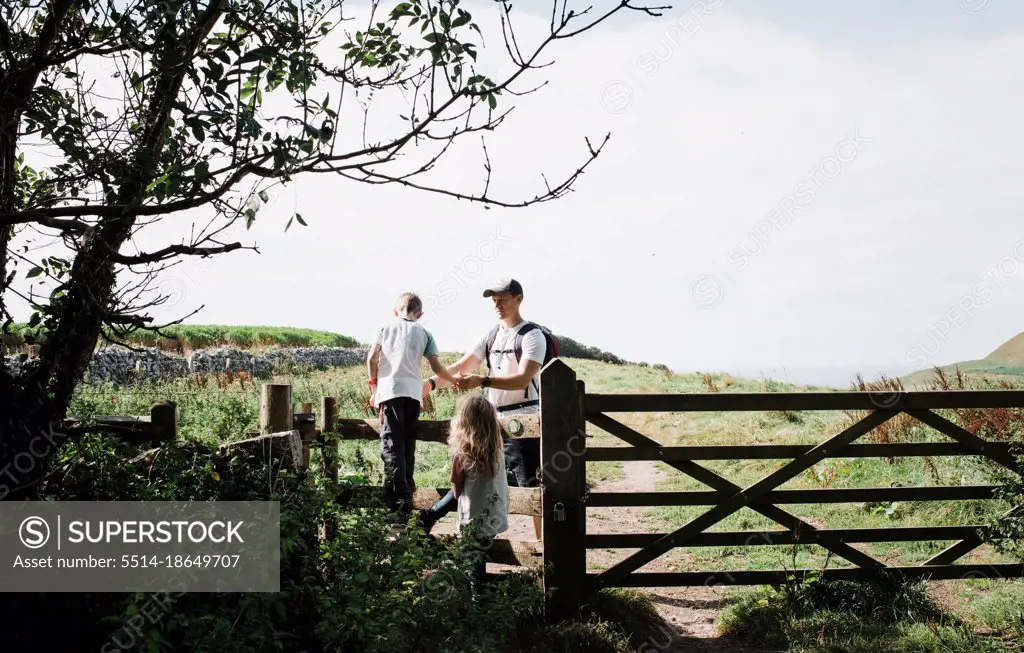 dad helping his kids climb over a stile in the english countryside