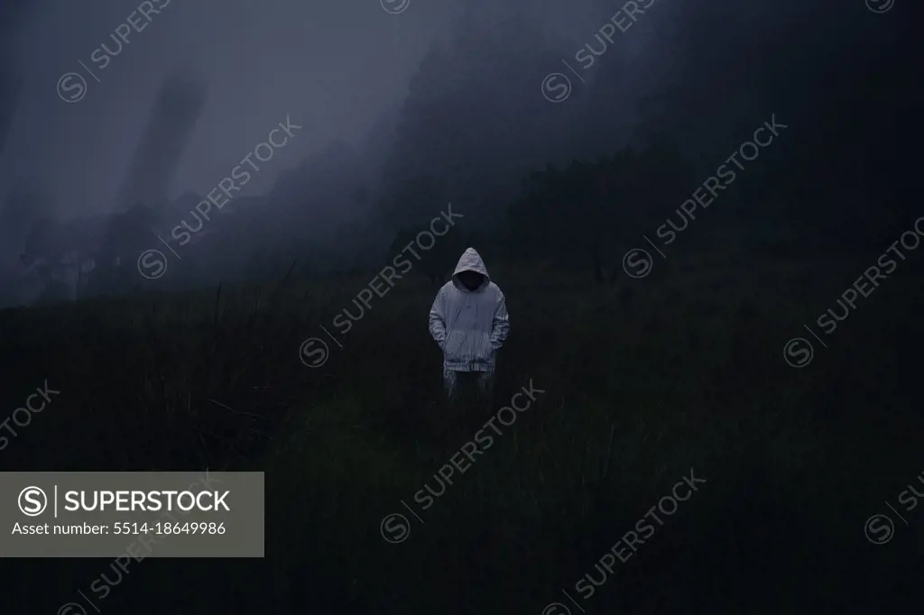 One mysterious man wearing a white hoodie in dark foggy forest