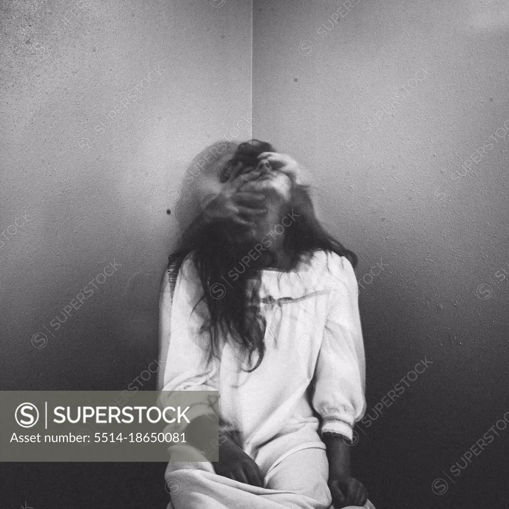 Spooky girl sitting in corner with hands pulling her face back