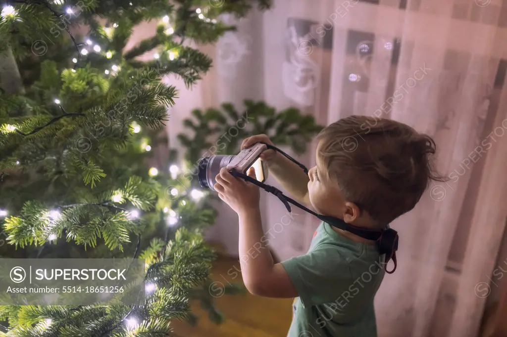 small toddler boy taking photos with camera of a christmass tree