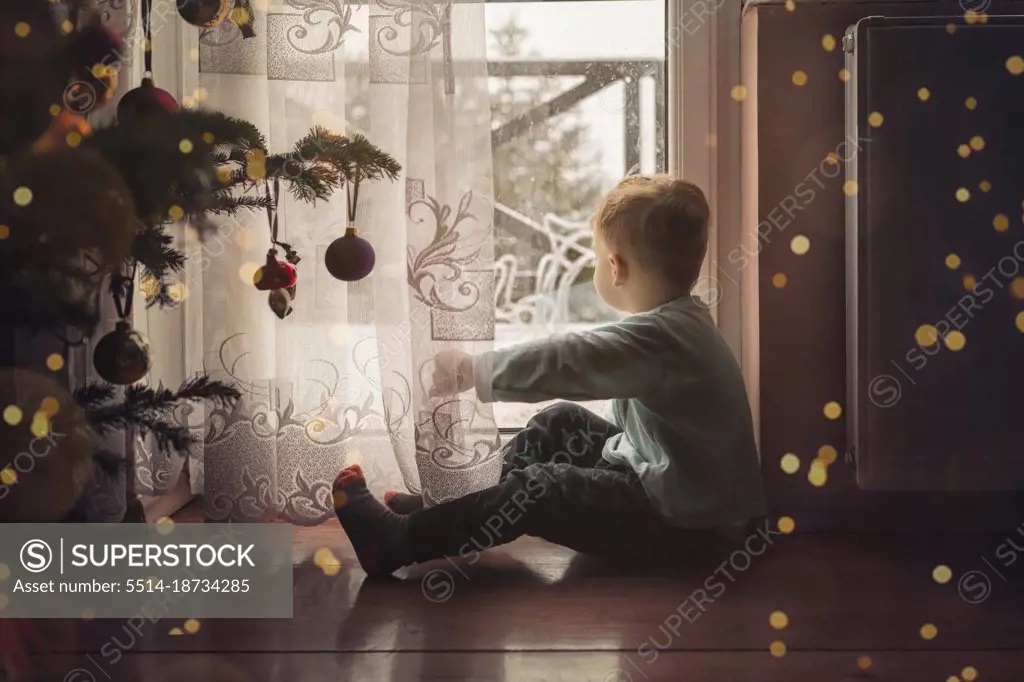 Toddler boy sitting on the floor by the window next to a christm