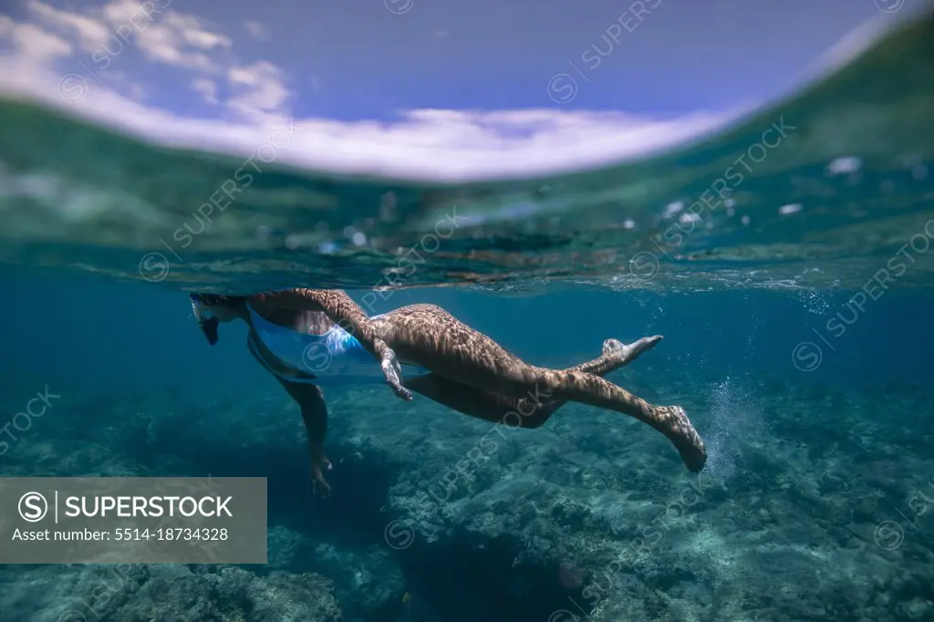 Female swims underwater in blue Hawaiian waters