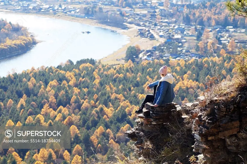 A female tourist sits on a sheer cliff on the bank of the Irkut River