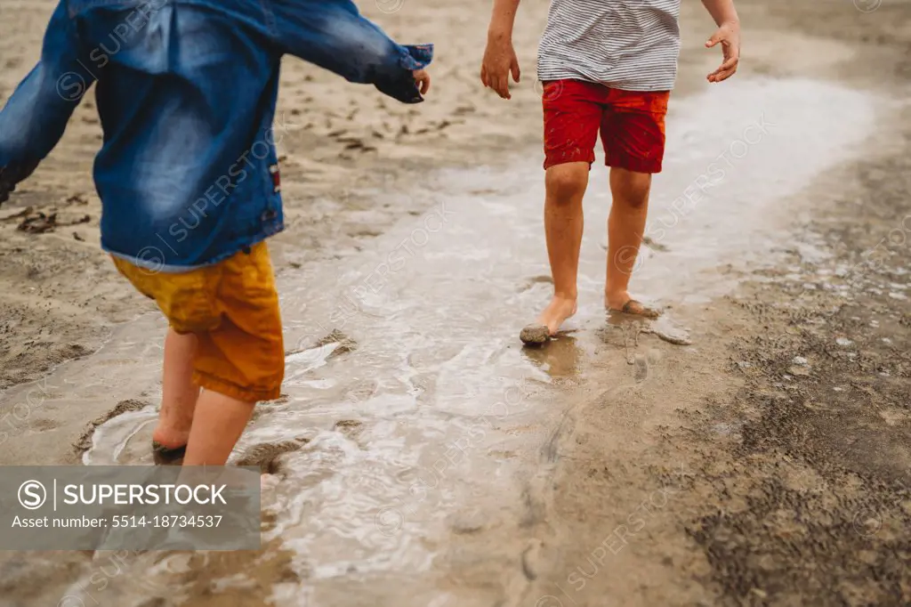 Young children putting feet under wet sand at beach