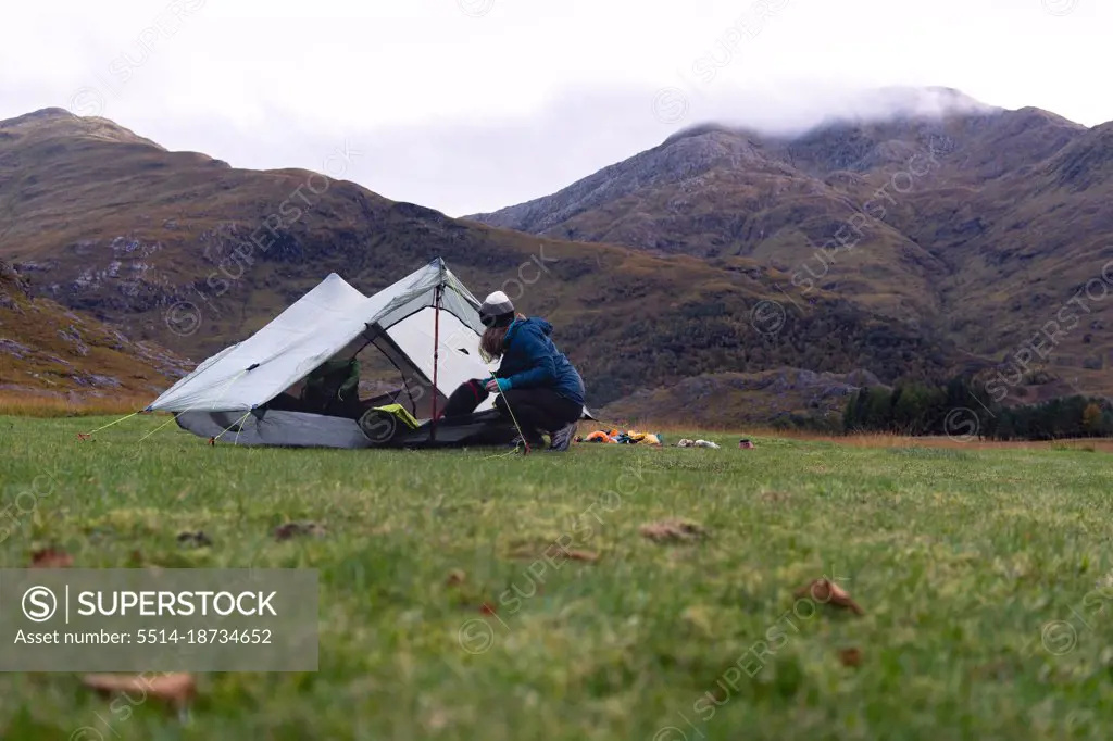 Female Camper setting up tent at foot of mountain