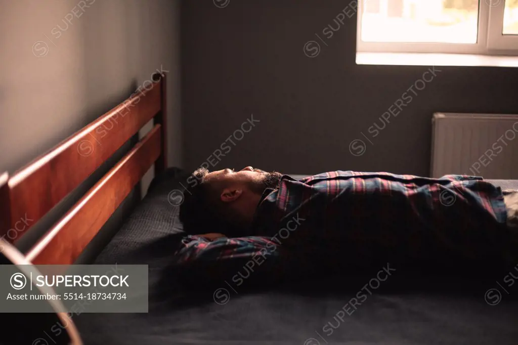 Thoughtful man looking through window lying on bed at home