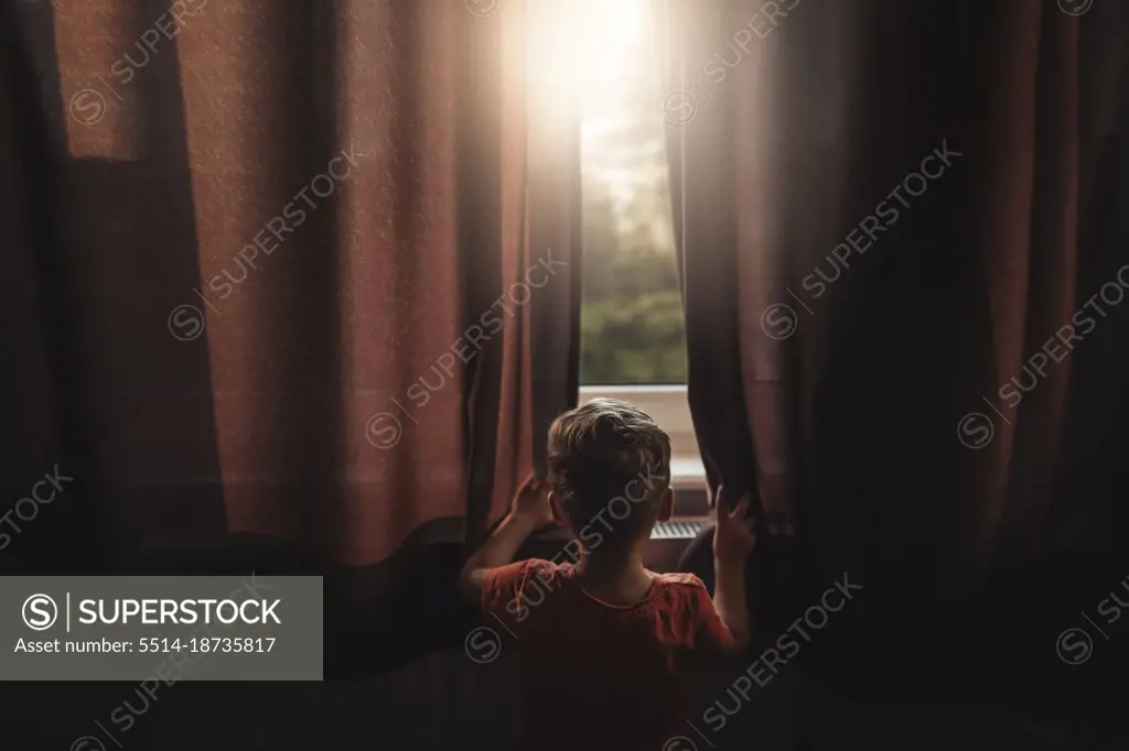 Back view of boy peaking outside through windows