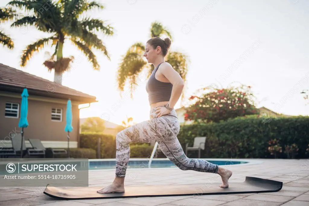 A woman doing mat pilates next to a pool at sunrise in the summer