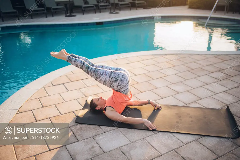 A woman doing mat pilates next to a pool at sunrise in the summer