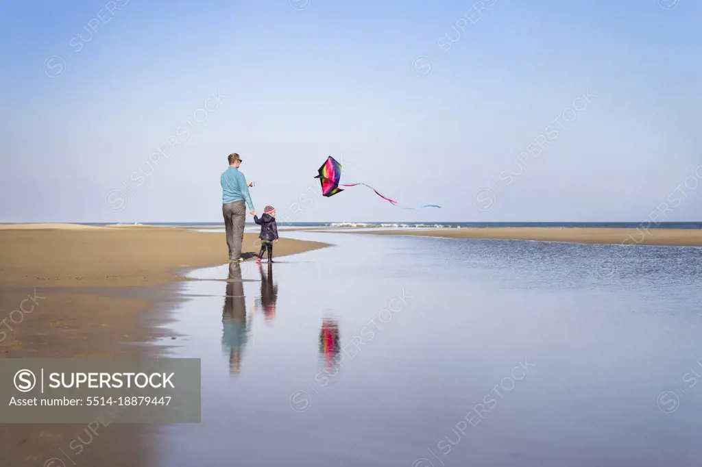 Father and daughter fly kite at beach in winter