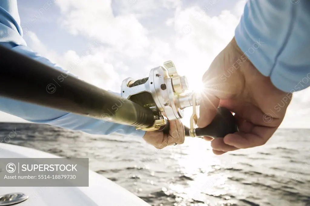 Close up shot of mans hands reeling in fishing rod with sunburst