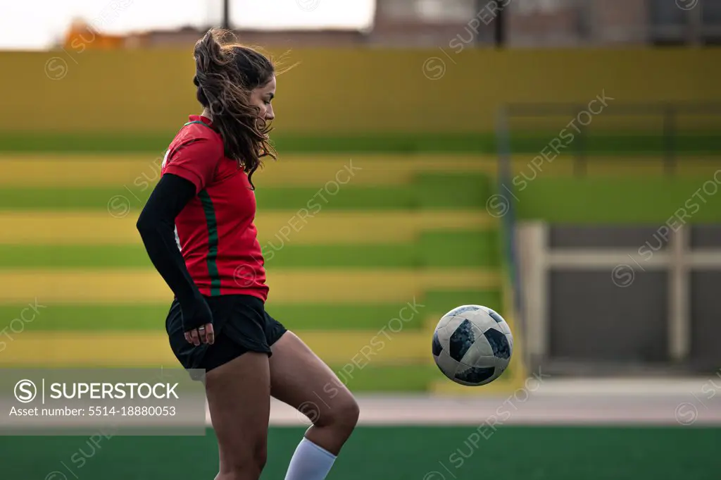 Young female soccer player kicks the ball on the field