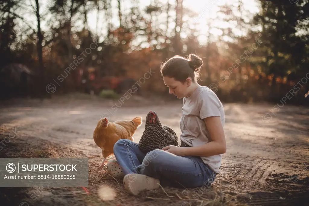 Girl sitting on dirt driveway with chickens