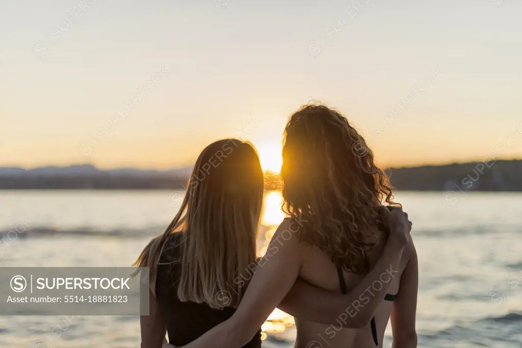 Latin girlfriends watching the sunset together at summer lake