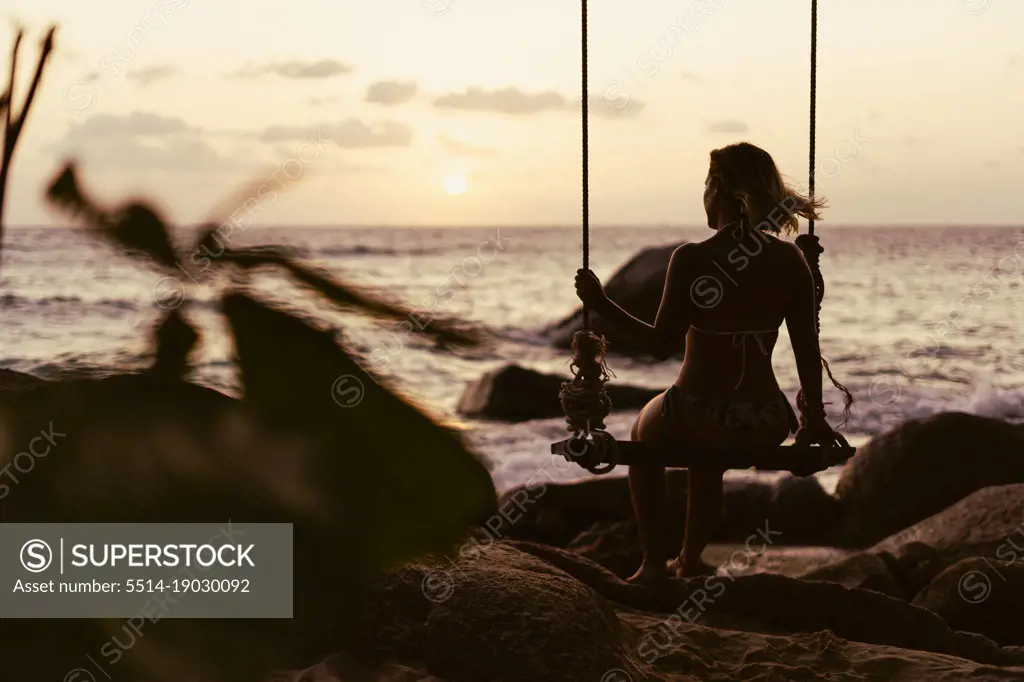 Silhouette of a happy girl swinging on a tropical beach surrounded