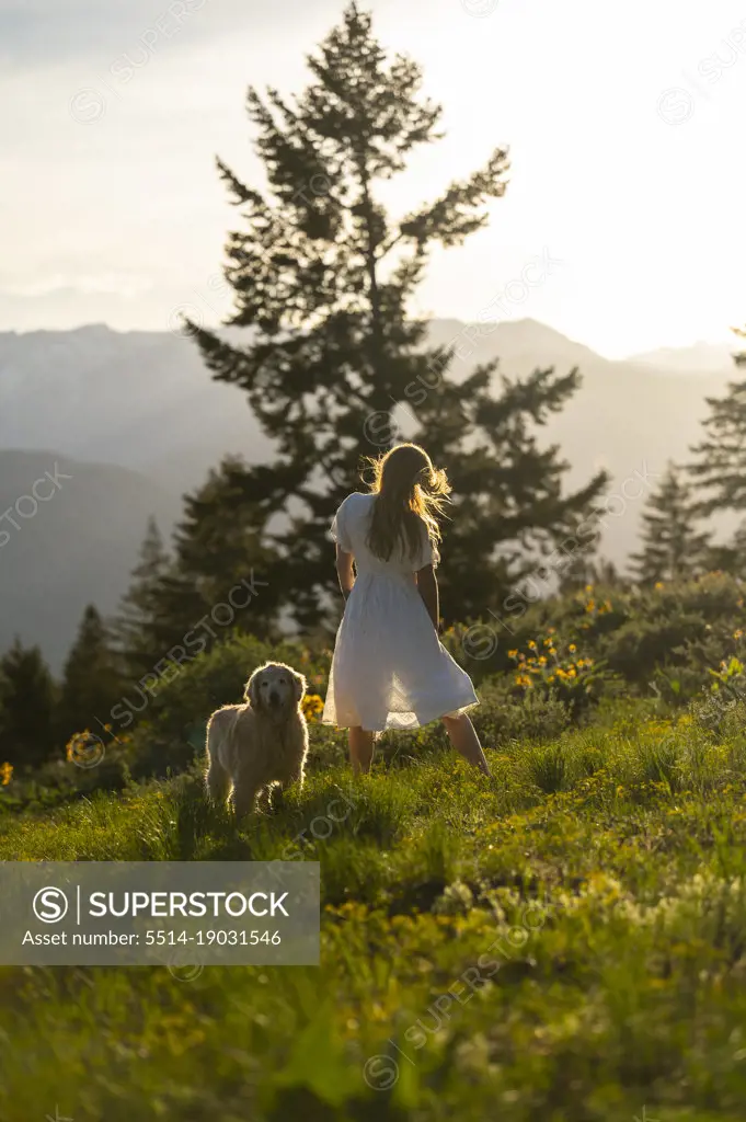 Female in a dress standing with her dog in the mountains