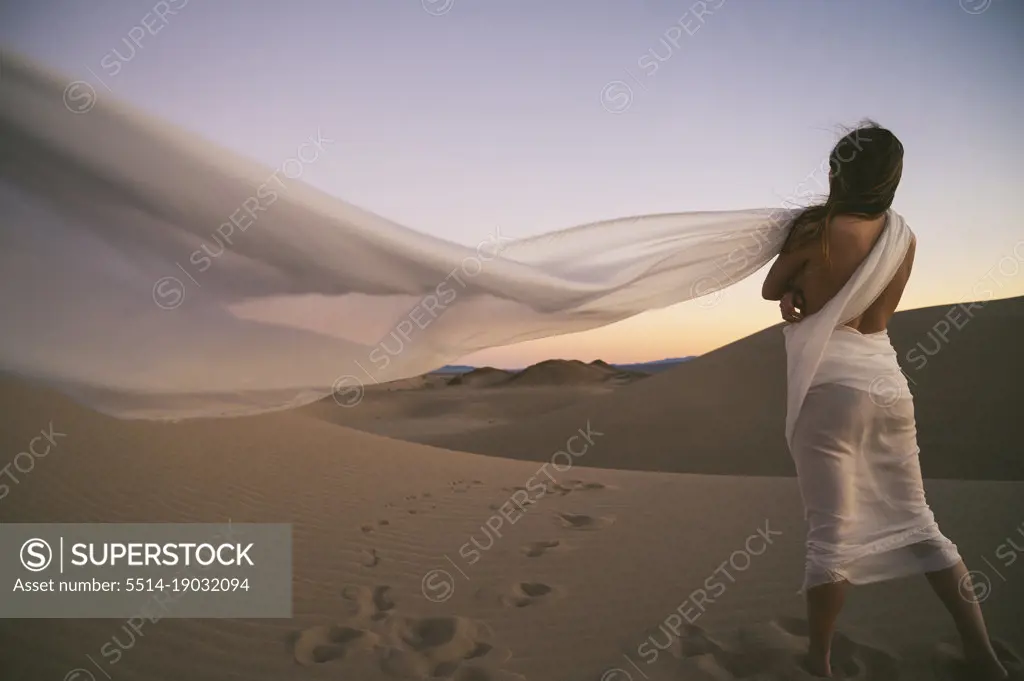 Naked female posing on a sand dune wrapped in a white cloth