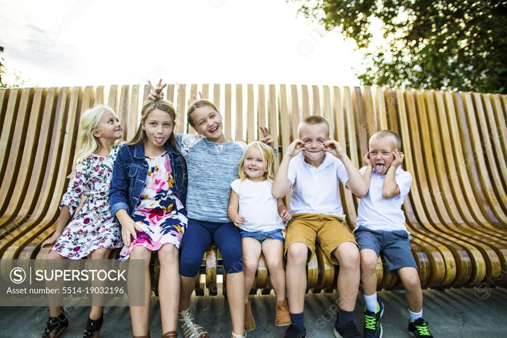 Six siblings making funny faces together outdoors.