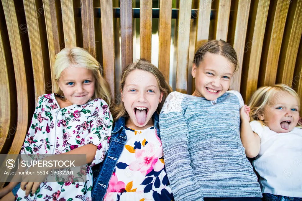 Playful portrait of four cute young girls on wooden bench.