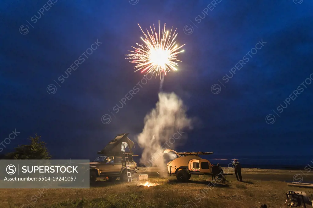 Fireworks go off above a beach with camping trailer and camp truck