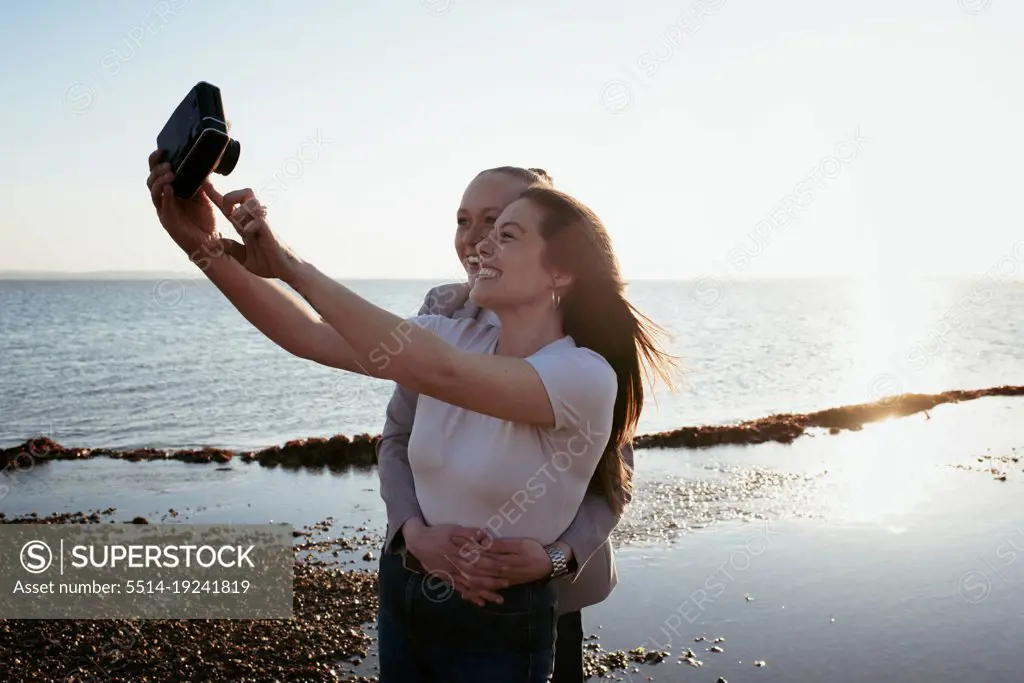 lesbian couple taking selfies at the beach at sunset