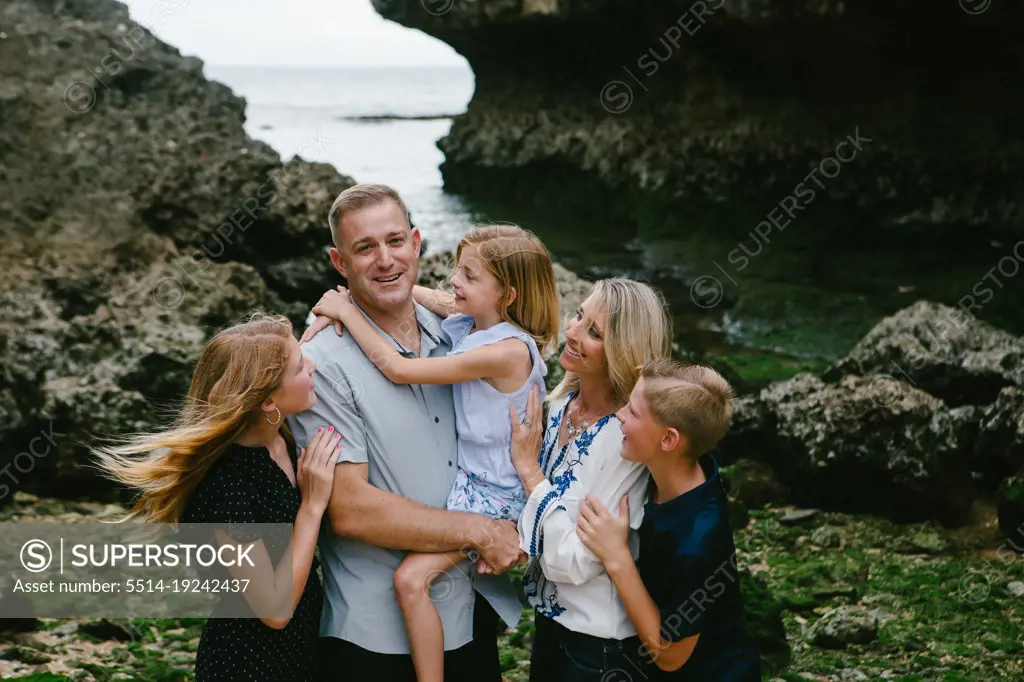 Family of five hugs and laughs together on tropical beach