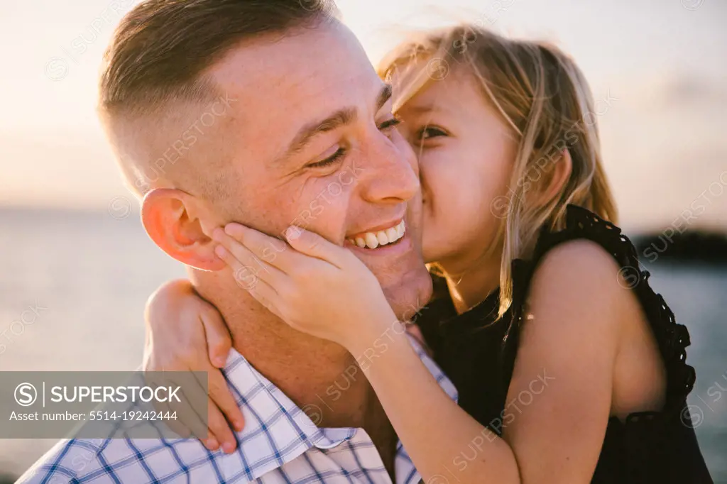 5 year old daughter gives father a kiss on the cheek by ocean