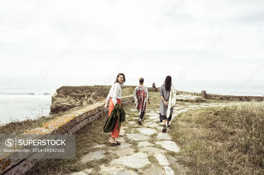 Group of alternative friends walk along coast in summer