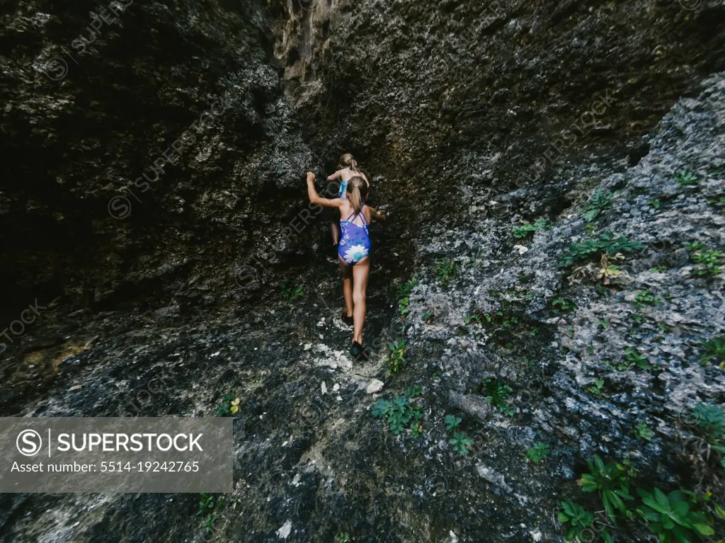 Two blond seven year old girls hike on tropical lava rock on vacation