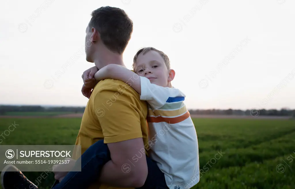 father giving son piggy back ride wjilst walking at sunset