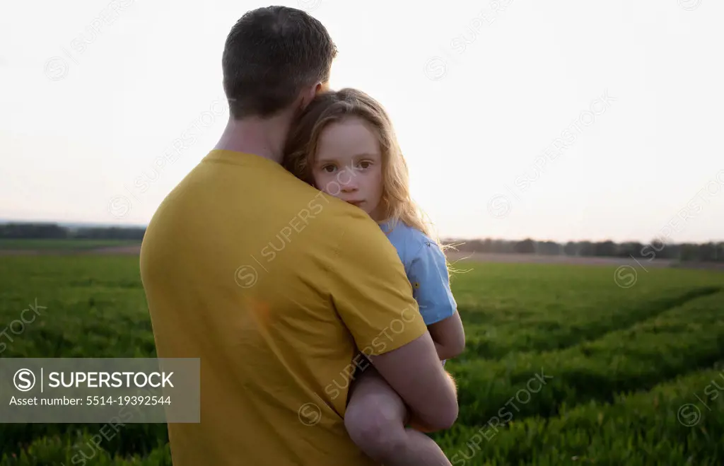 father carrying a tired daughter through a field at sunset