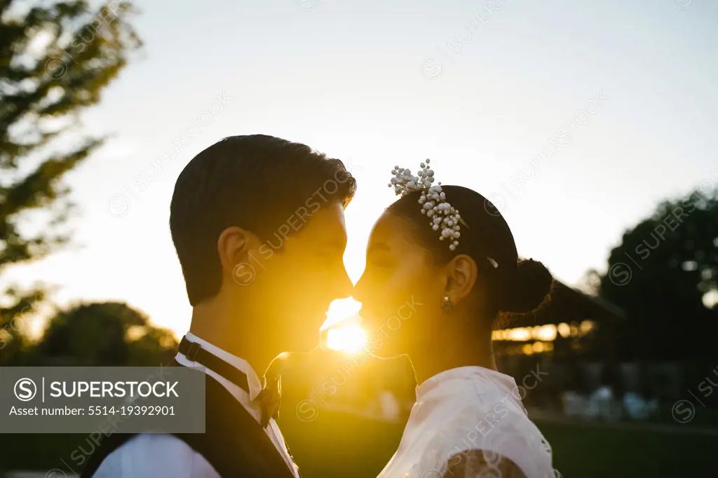 Multiracial couple touch noses in loving embrace with sunset