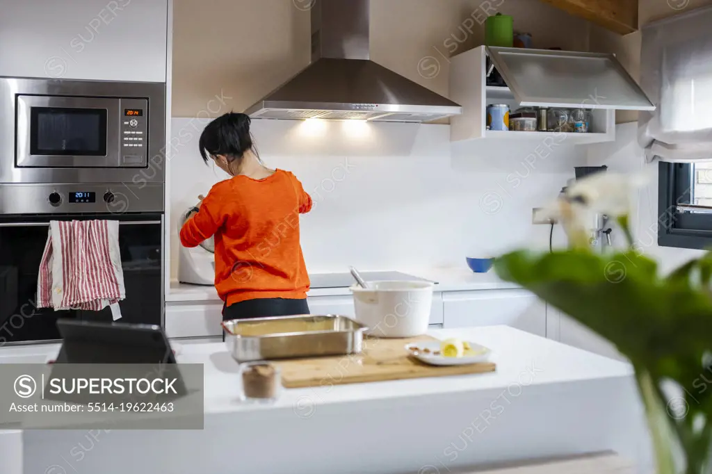 Rear view of a woman at kitchen while preparing a cake