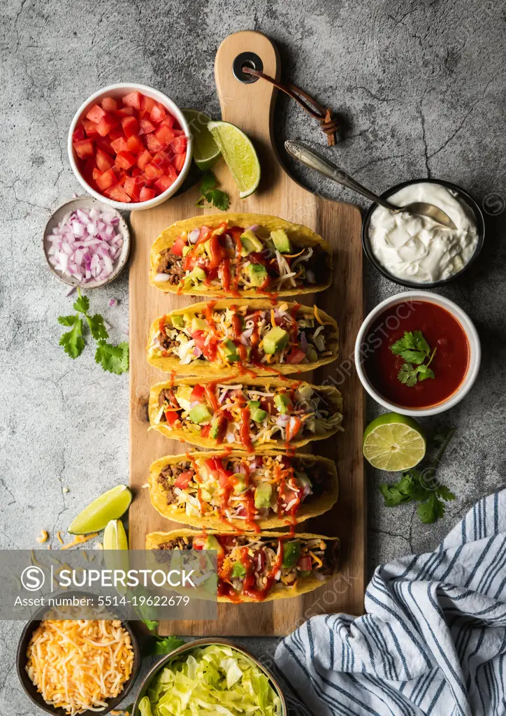 Hard shell tacos on wooden board with beef, lettuce, tomatoes, cheese.